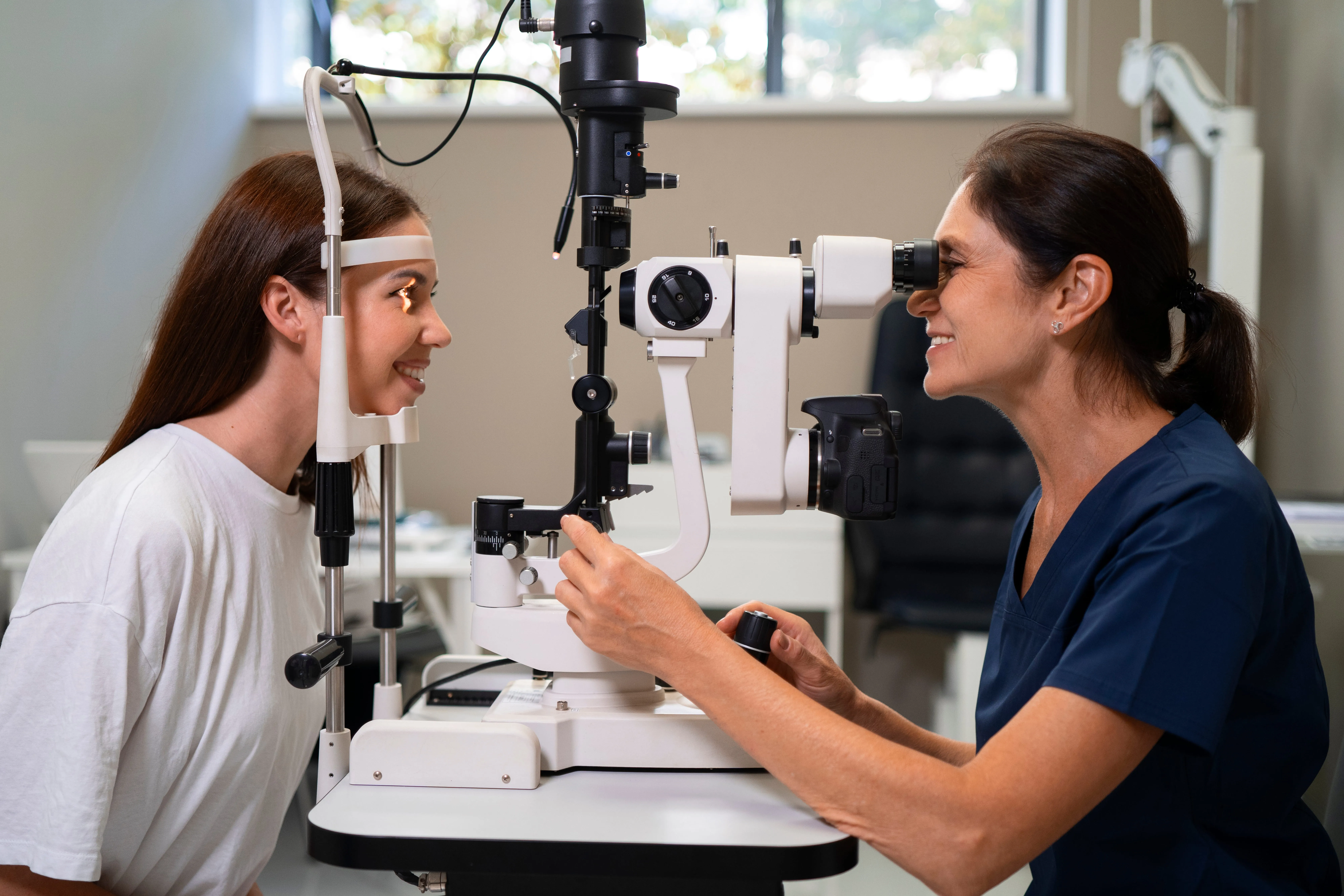 Optometrist examines patient's eyes using slit lamp equipment in medical office.