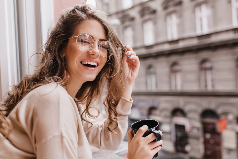 Smiling woman with glasses holding coffee cup near historic building.