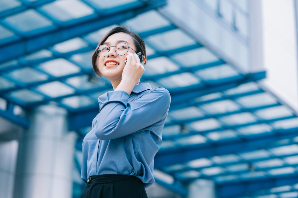 Woman in glasses and blue shirt talking on phone in modern office building