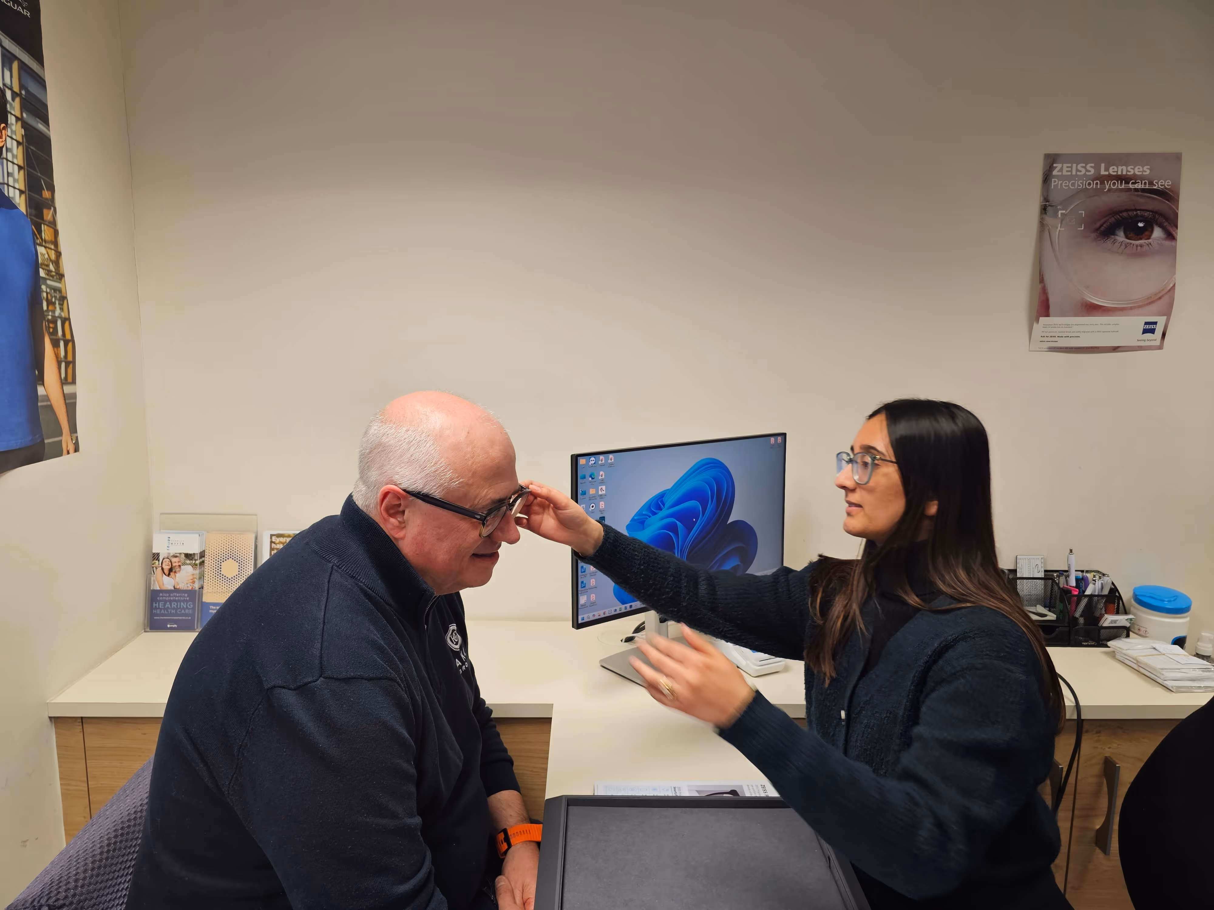 Optometrist fitting glasses on elderly male patient in eye care clinic office