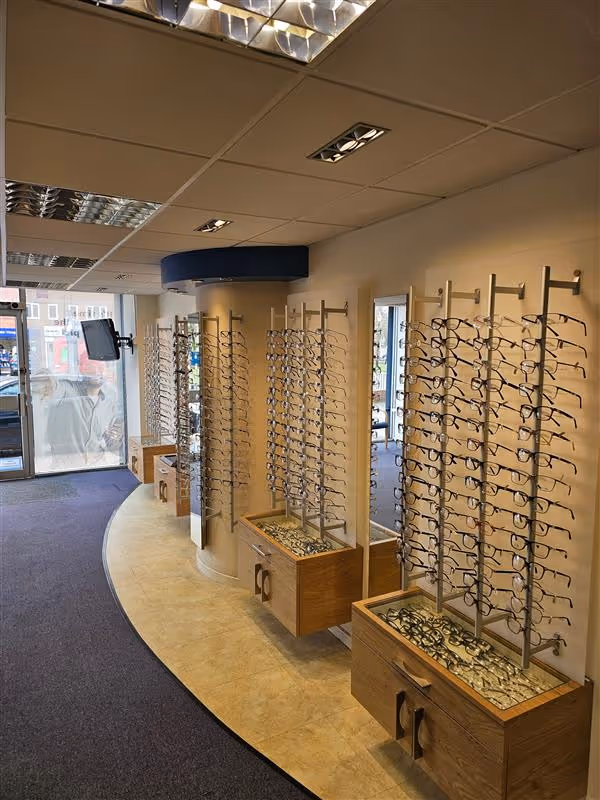 Eyeglasses display stands with multiple frames arranged on wooden holders in optometry shop interior.