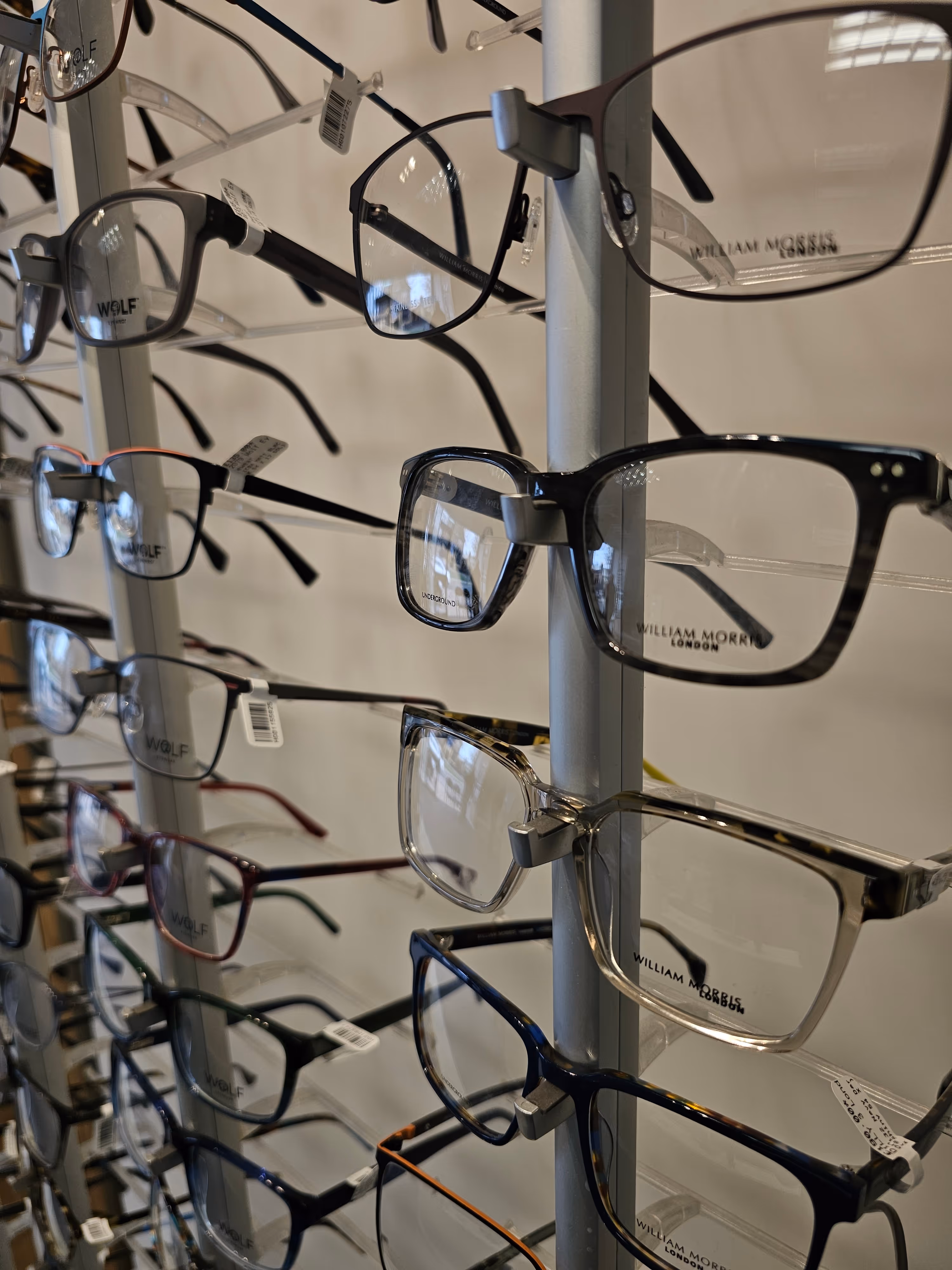 Display of various eyeglasses and frames on a white stand in a retail shop.