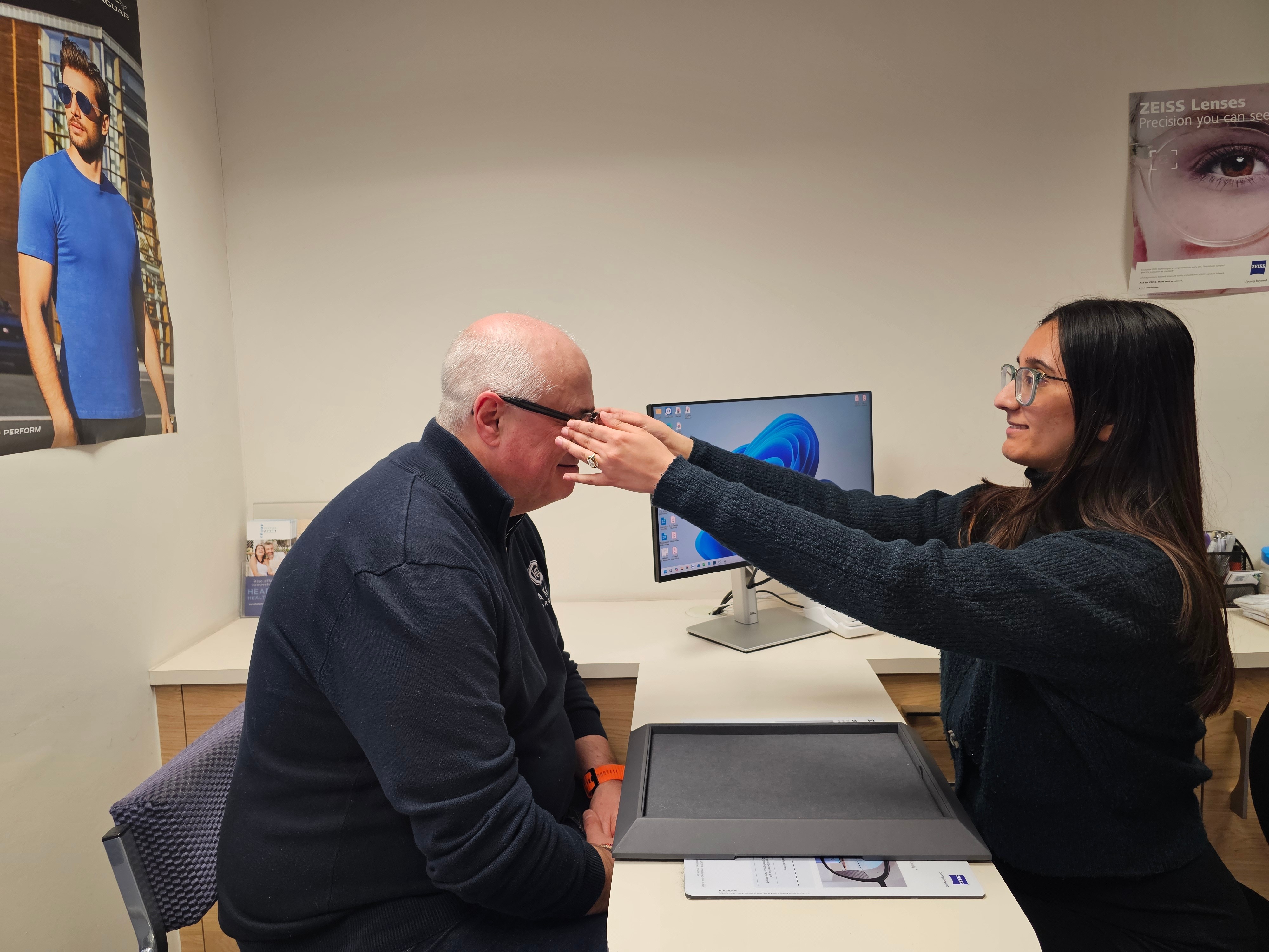 Optometrist fitting glasses on older man at desk in modern eye care office