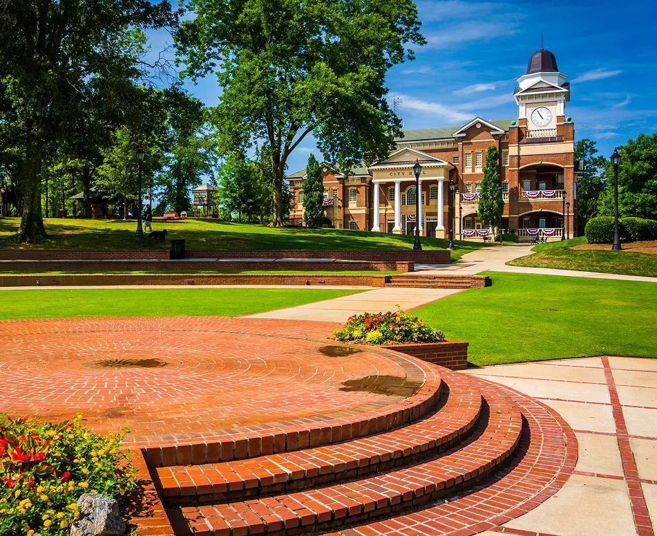 A brick circular plaza with steps leading up to a lawn and a large city hall building with a clock tower under a bright blue sky.