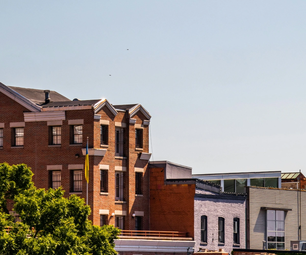 Multi-story brick and mixed-material buildings under clear sky with green trees in the foreground.