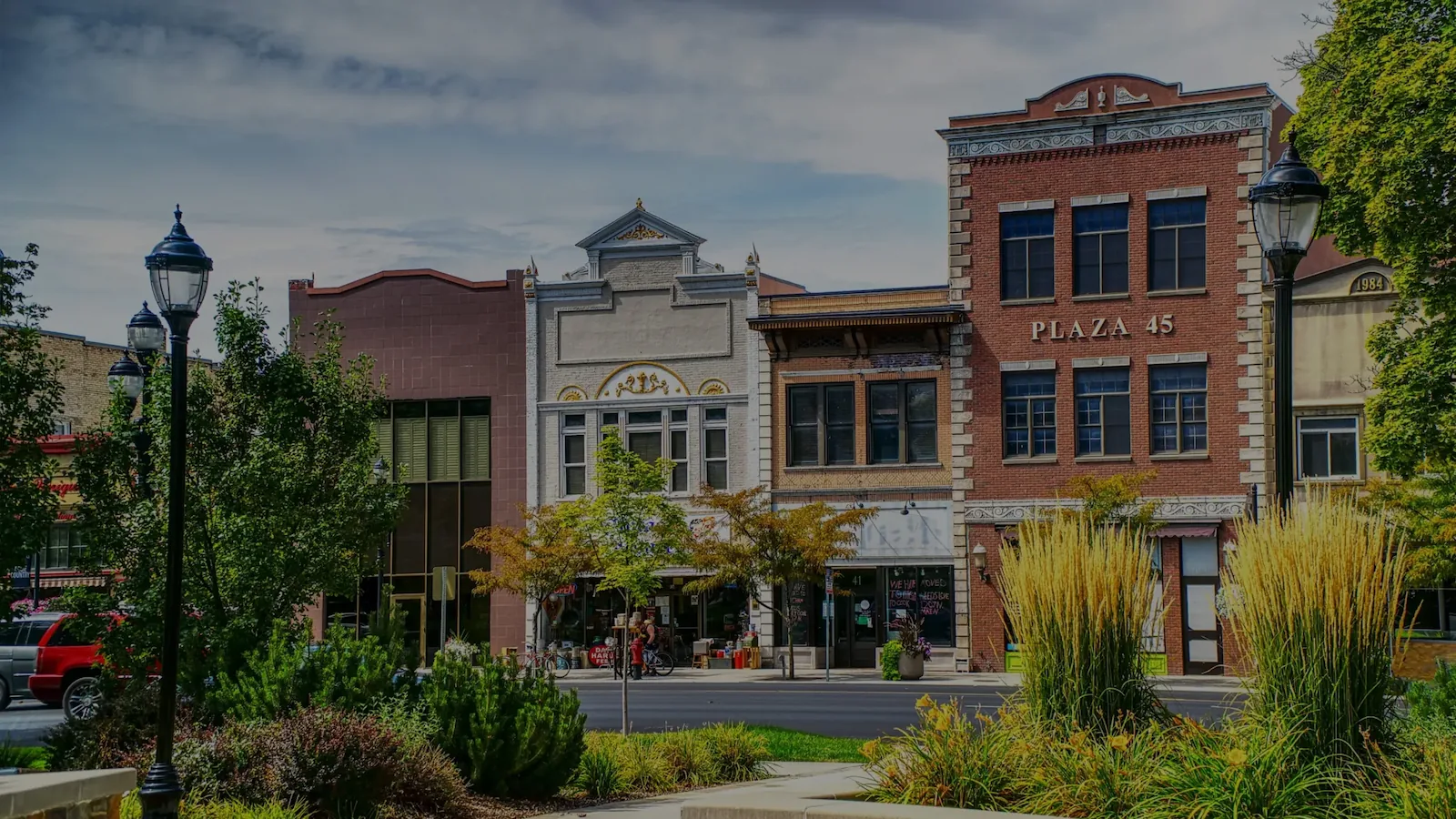 Street view of historic downtown buildings with greenery and vintage-style street lamps in the foreground.