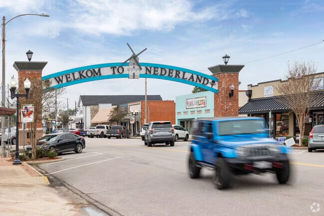 Street scene in Nederland with a blue arch reading 'Welkom to Nederland' and cars driving beneath it.