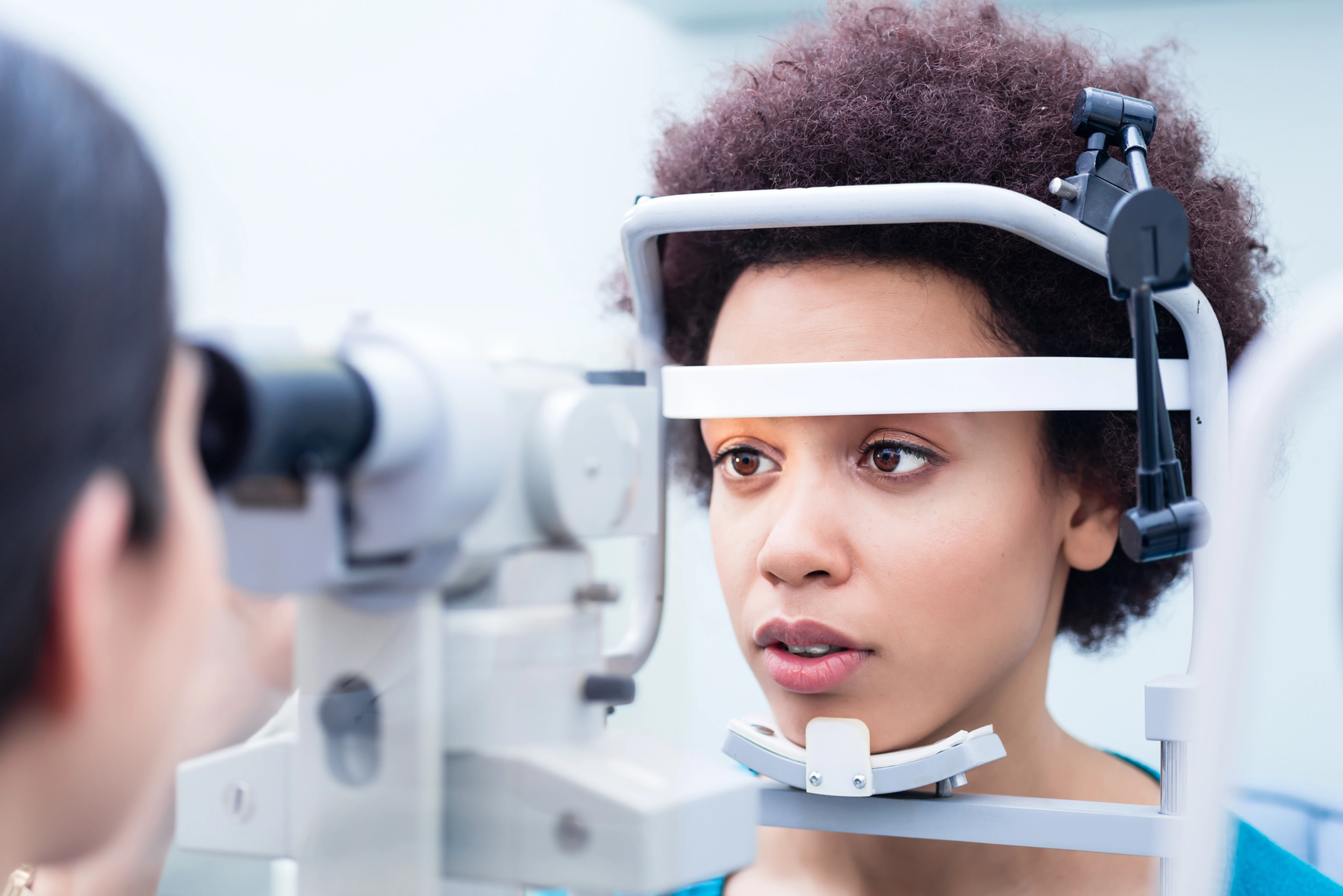 Woman undergoing eye exam using a slit lamp device by an eye care professional.