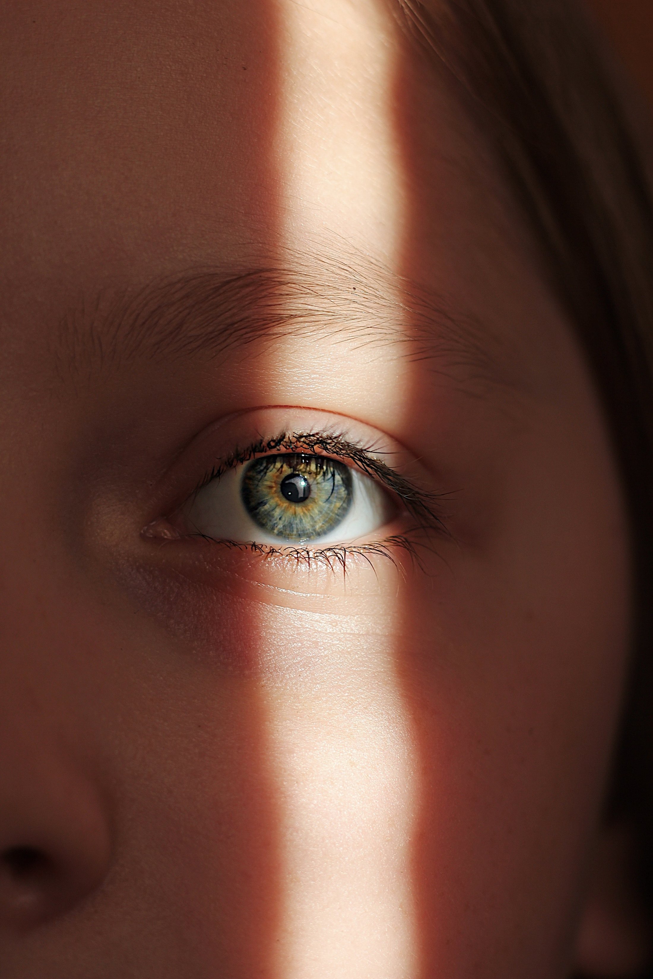 Close-up of a person's green eye partially illuminated by a narrow beam of sunlight.