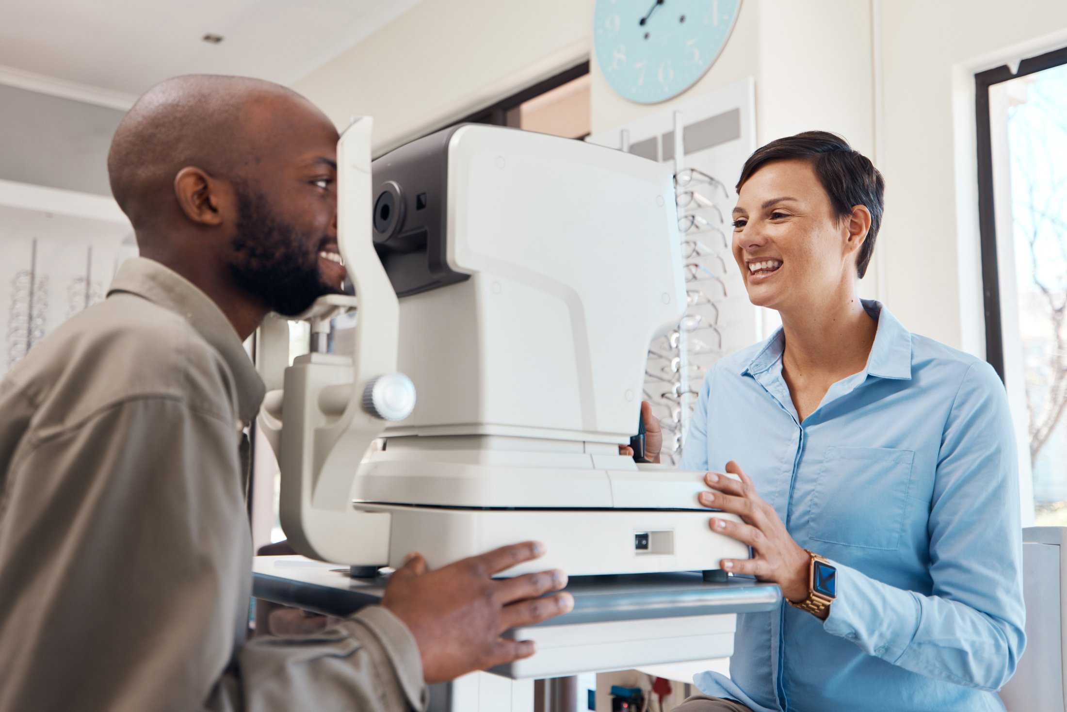 Optometrist smiling while examining patient's eyes using a diagnostic eye machine in a clinic.