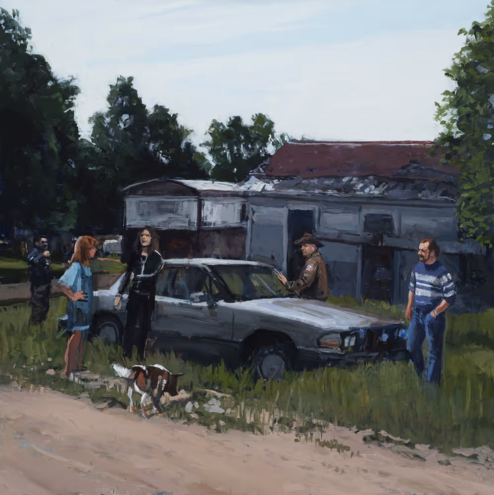 People standing around a silver car on grass near an old building and trees.