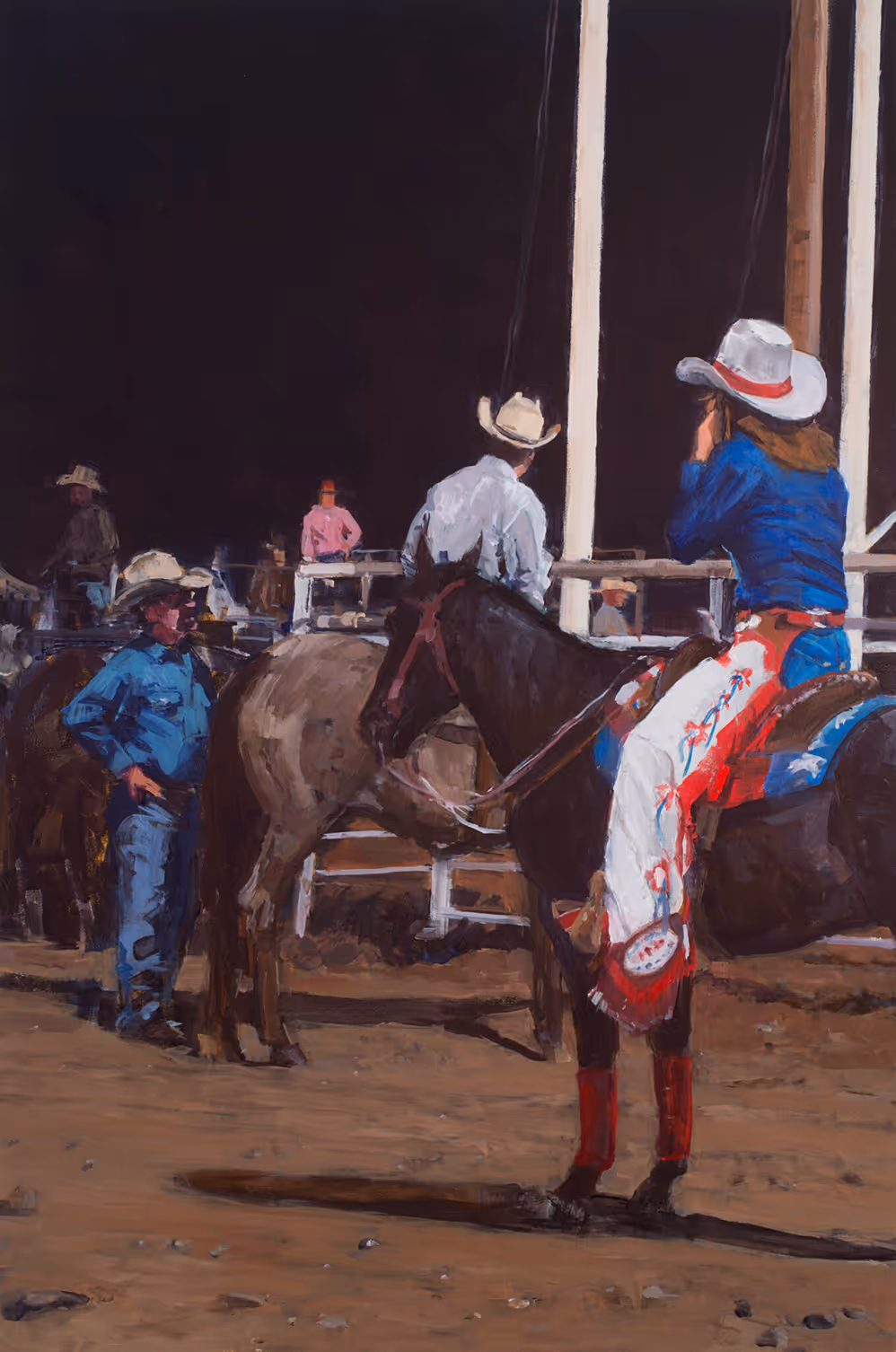 Cowboy and cowgirl in western attire with hats by horses in a rodeo arena at night.