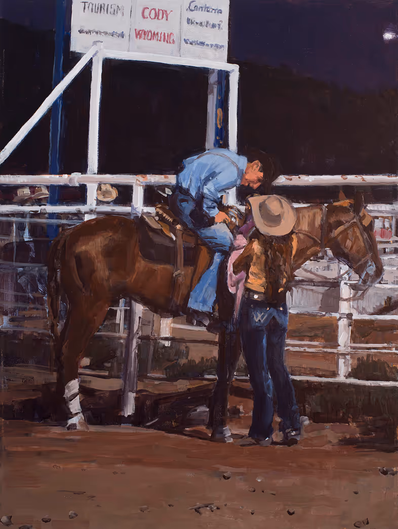 A man in blue clothing sits on a horse while a woman in a hat stands beside them in a rodeo setting.