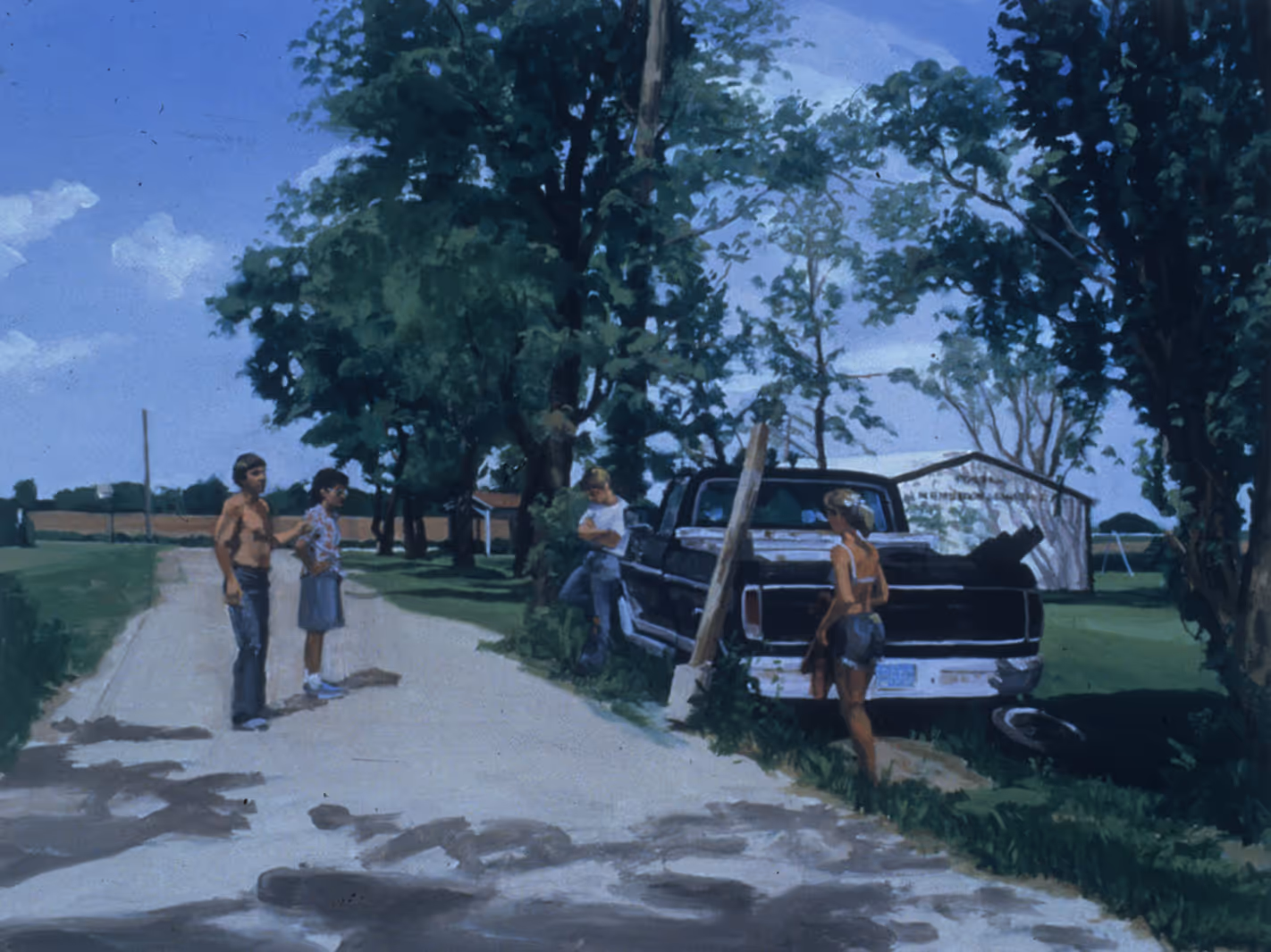 Four young people stand by a rural road near a pickup truck and trees on a sunny day.