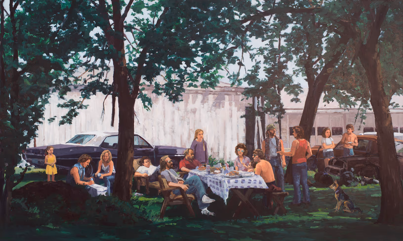 Group of people having a picnic under trees with cars and a dog nearby on grass.