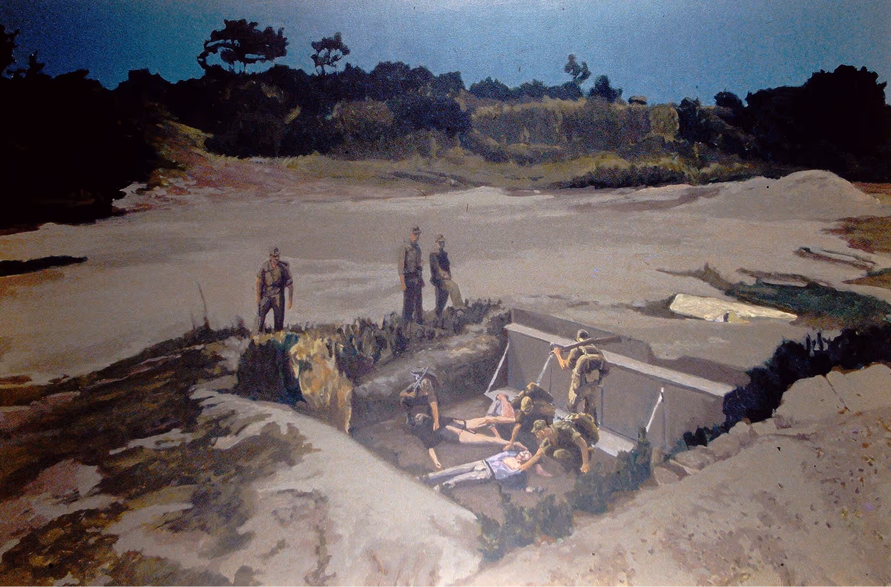 Several soldiers around a trench with two civilians lying inside, in an open barren landscape.