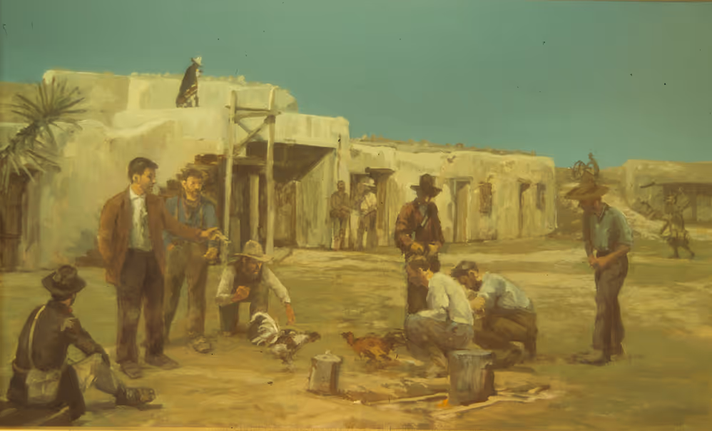 Group of men gathered outdoors around two roosters fighting near adobe buildings.