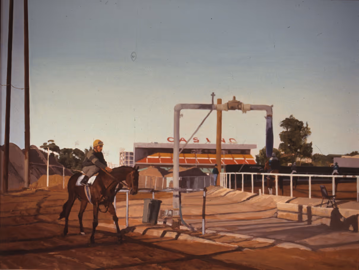 Jockey riding a horse on a racetrack near a building with a 'CASINO' sign during daytime.
