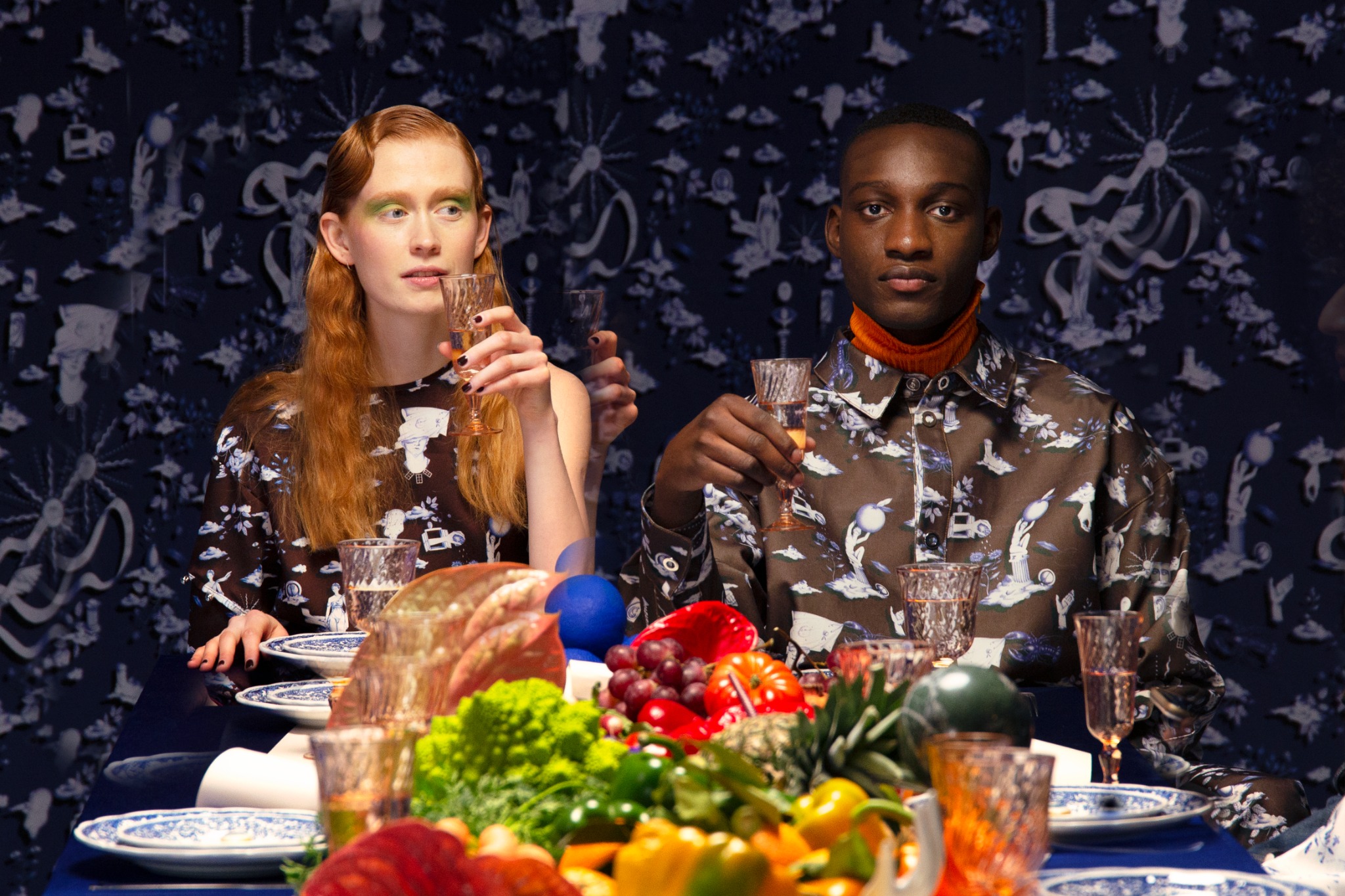 Two guests in printed shirts at a table laid with fruit and glassware