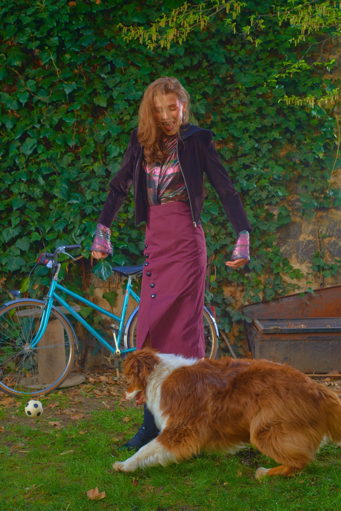 Model with a bicycle and a dog in front of a green hedge