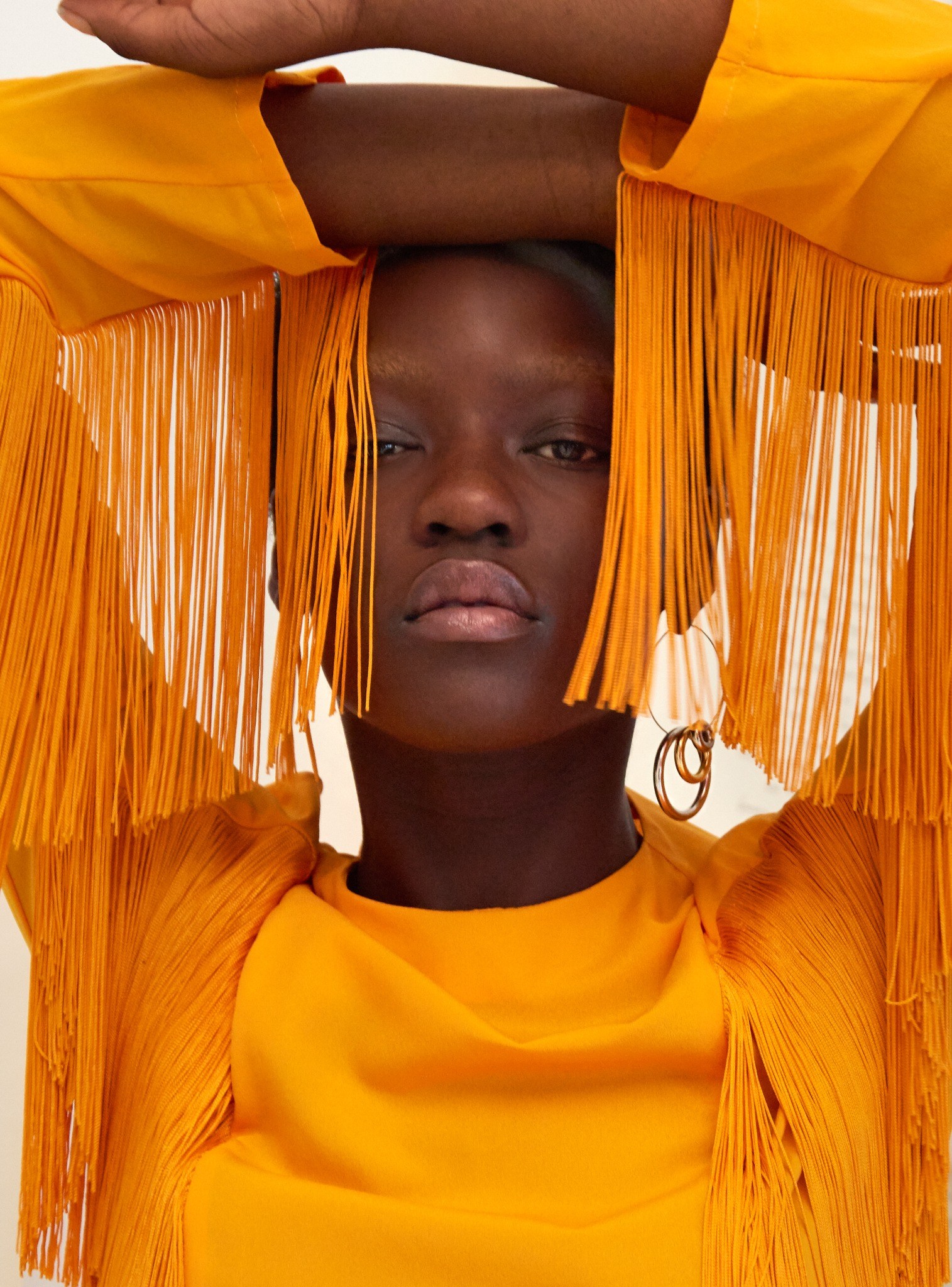 Model in white holding a white sphere beneath a pink fringed hat