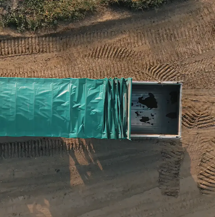 Luchtfoto van open vrachtwagen met groene dekking op een stoffige grond met bandenafdrukken.