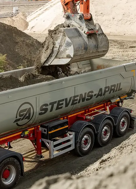 Graafmachine stort aarde in een STEVENS-APRIL kiepwagen op een bouwplaats.