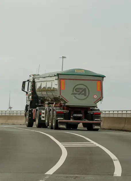 Vrachtwagen met een grote zilveren laadbak rijdt op een bochtige snelweg.