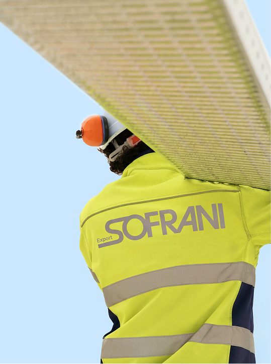 Worker wearing a yellow jacket with 'SOFRANI Export' printed on the back and carrying a metal ladder over their shoulder.