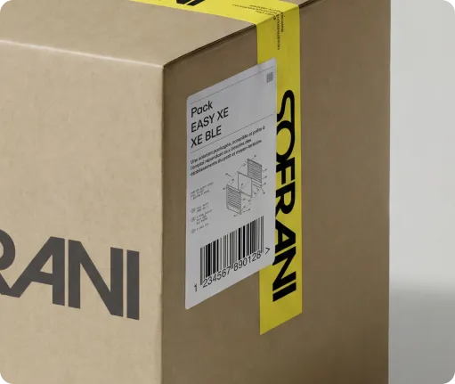 Close-up of a brown cardboard box sealed with yellow tape labeled SOFRANI and a label showing pack details and barcode.