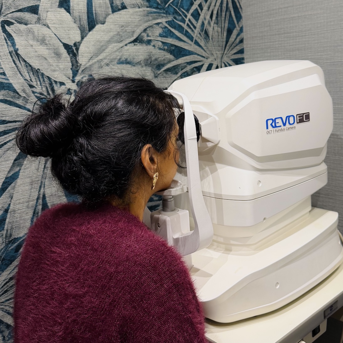 Woman using Revo FC OCT fundus camera for eye examination in medical office