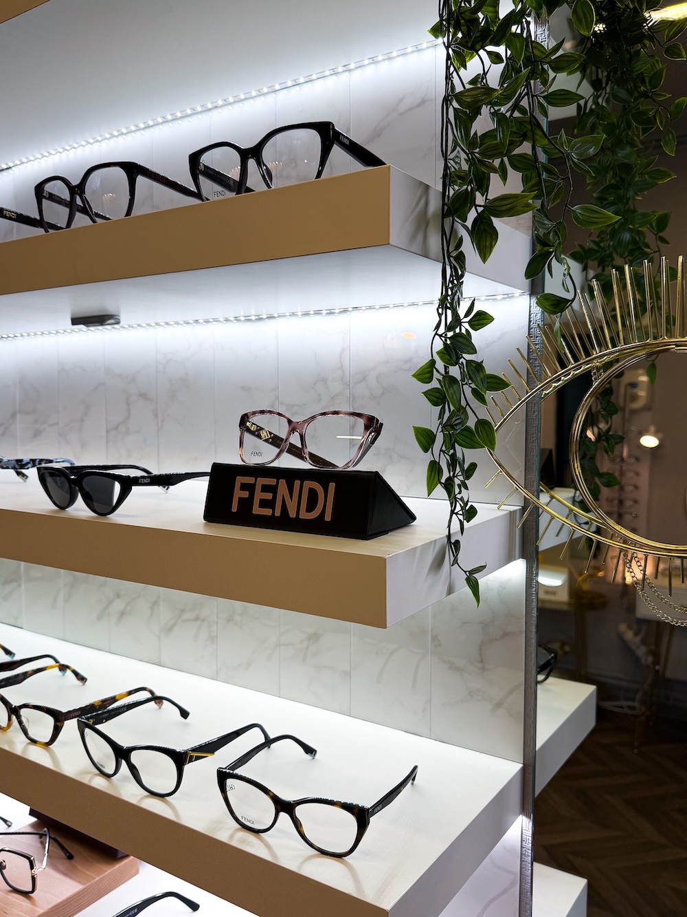 Luxury eyewear display showcasing Fendi glasses and sunglasses on white shelves with decorative plants.