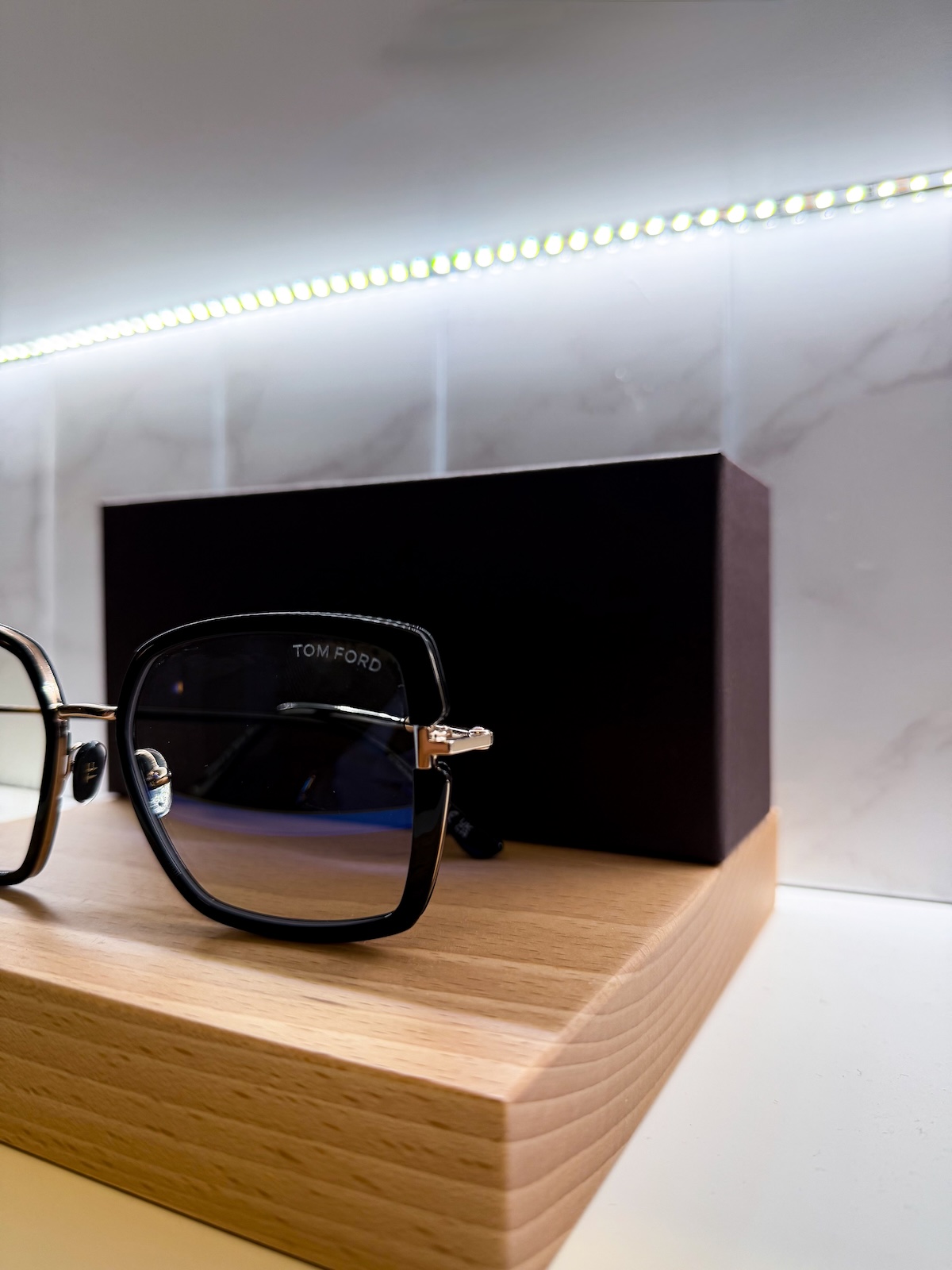 Tom Ford black framed sunglasses displayed on wooden display block with LED lighting