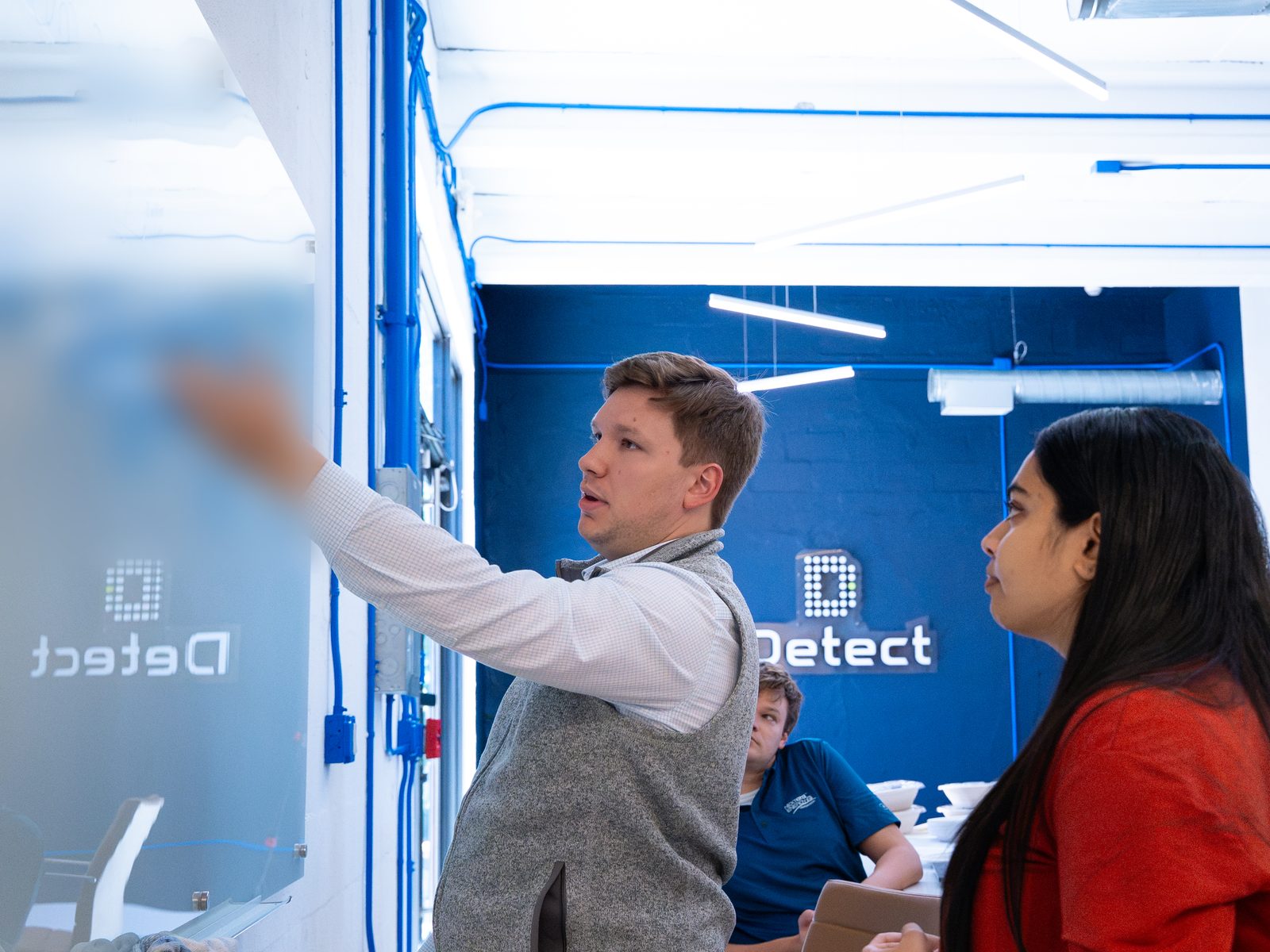 Hackathon teammates walk through whiteboard planning notes at the Detect office - notes blurred for confidentiality