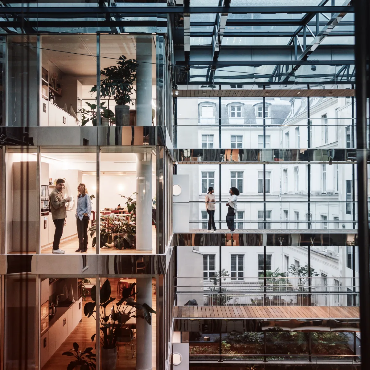 Two pairs of people talking inside and outside a modern building with glass walls and visible plants.