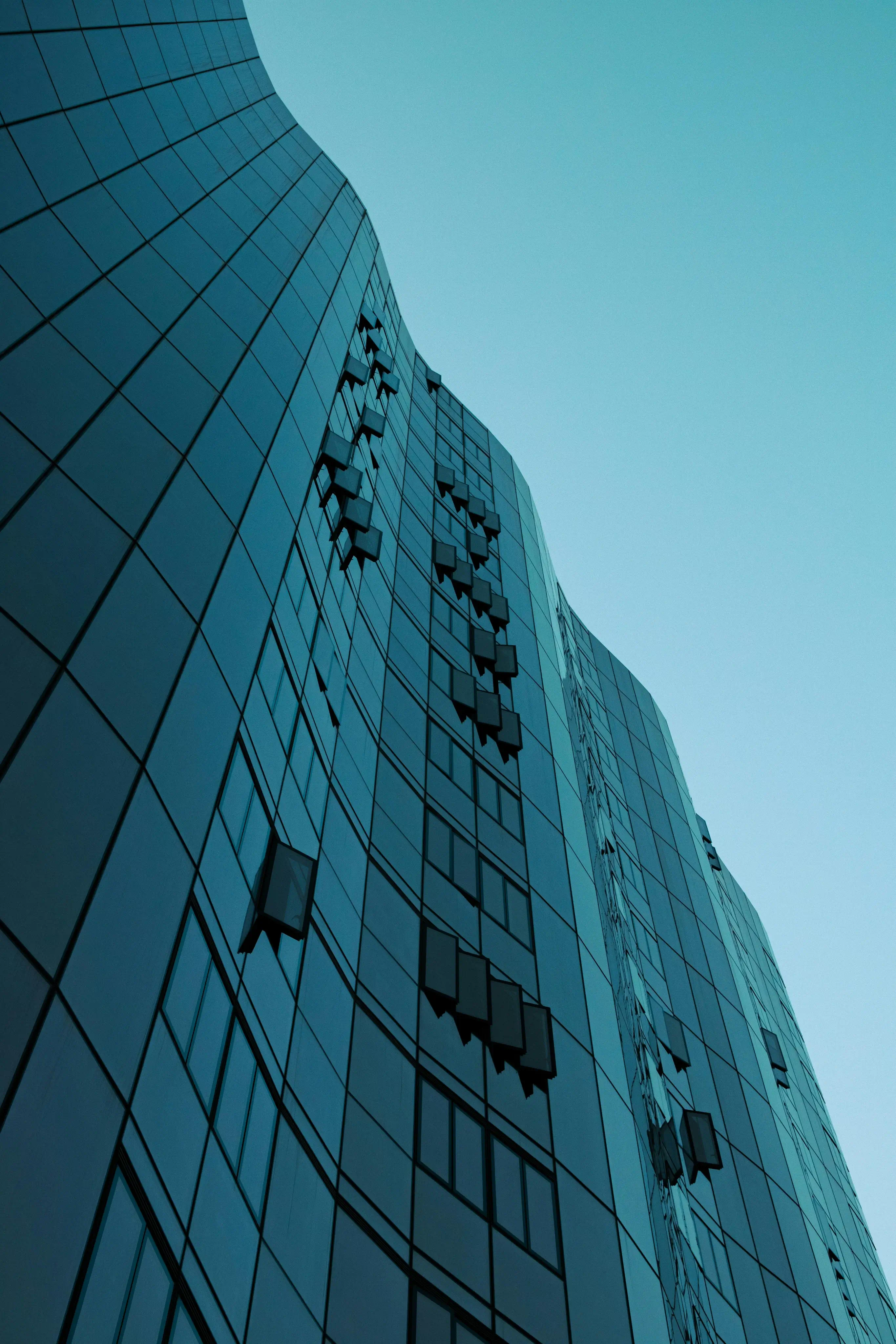 Low-angle view of a modern glass building with several open windows against a clear blue sky.