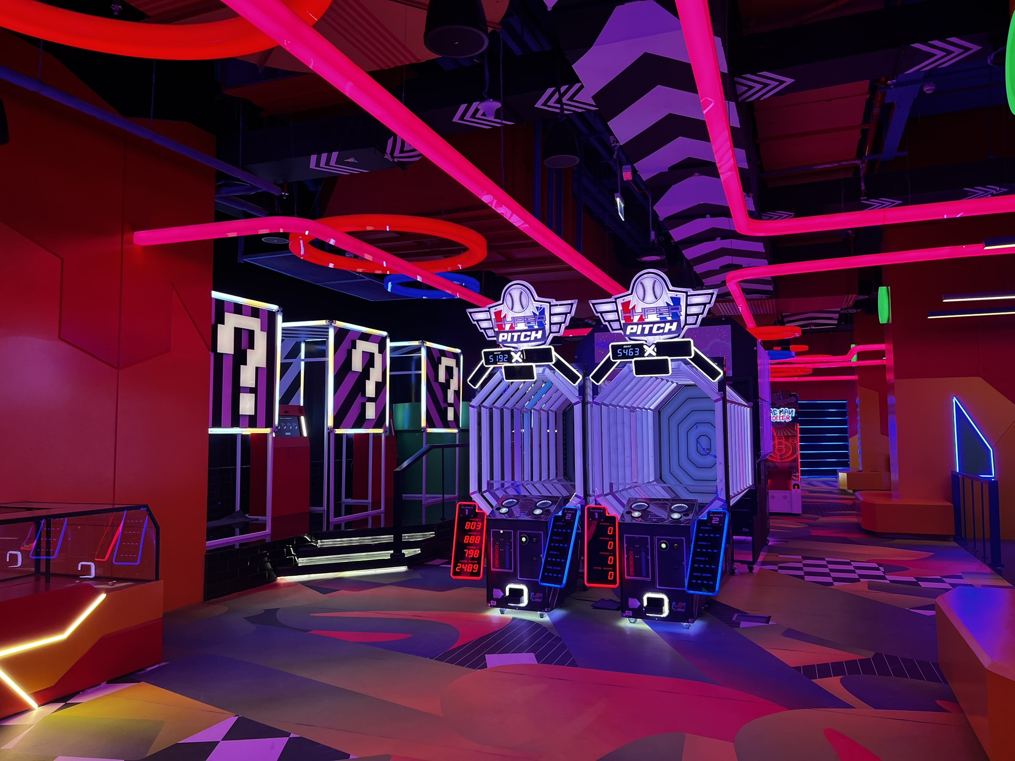 An arcade interior dominated by hot pink neon strip lighting on the ceiling.