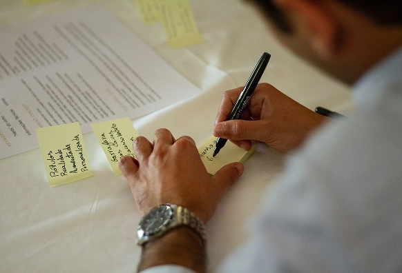 Fotografia de uma pessoa a escrever ideias em post-its amarelos, durante uma sessão de ideação.