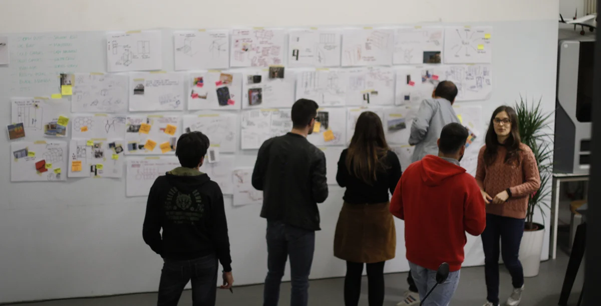 Fotografia de um aglomerado de pessoas a discutir o projeto com um quadro branco.
