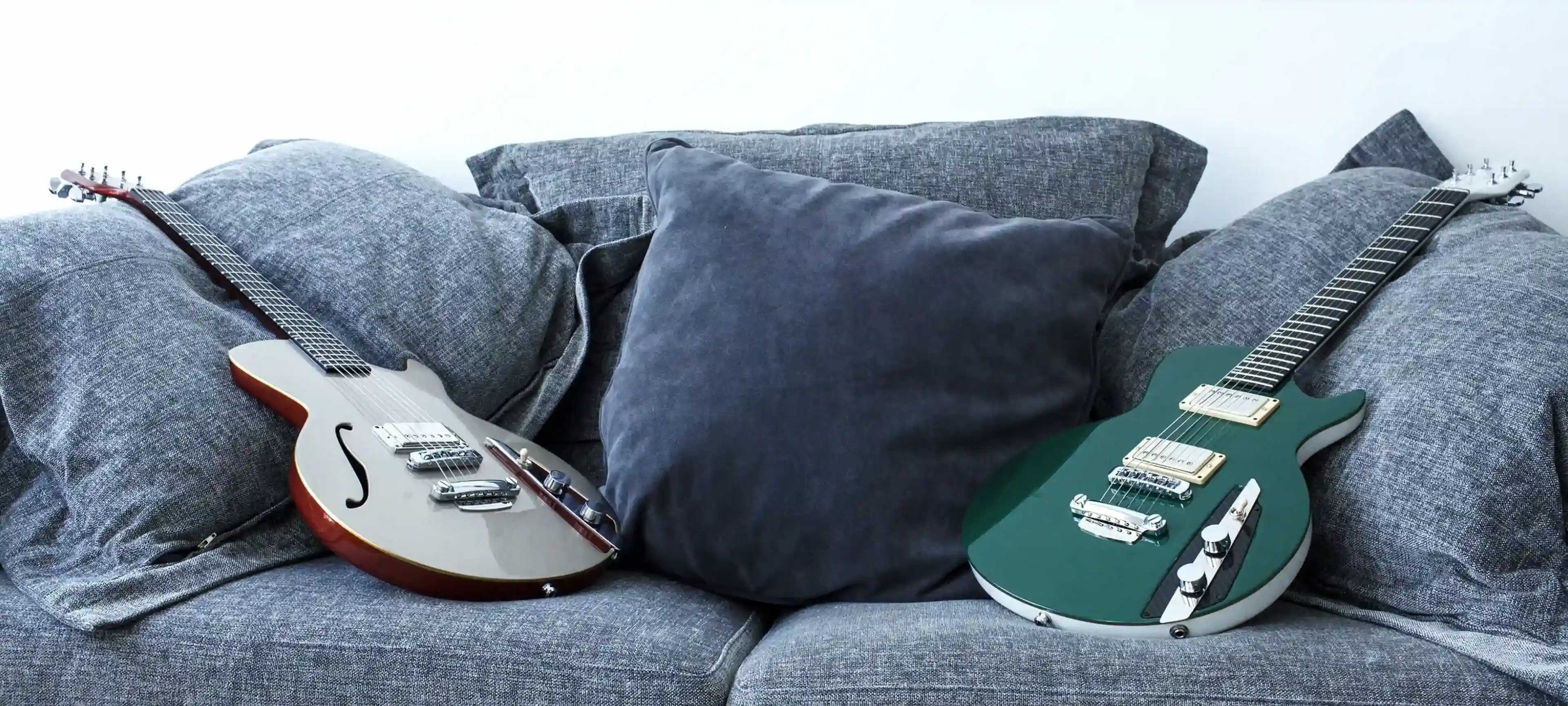 Fotografia de duas guitarras posicionadas em cima de um sofá.