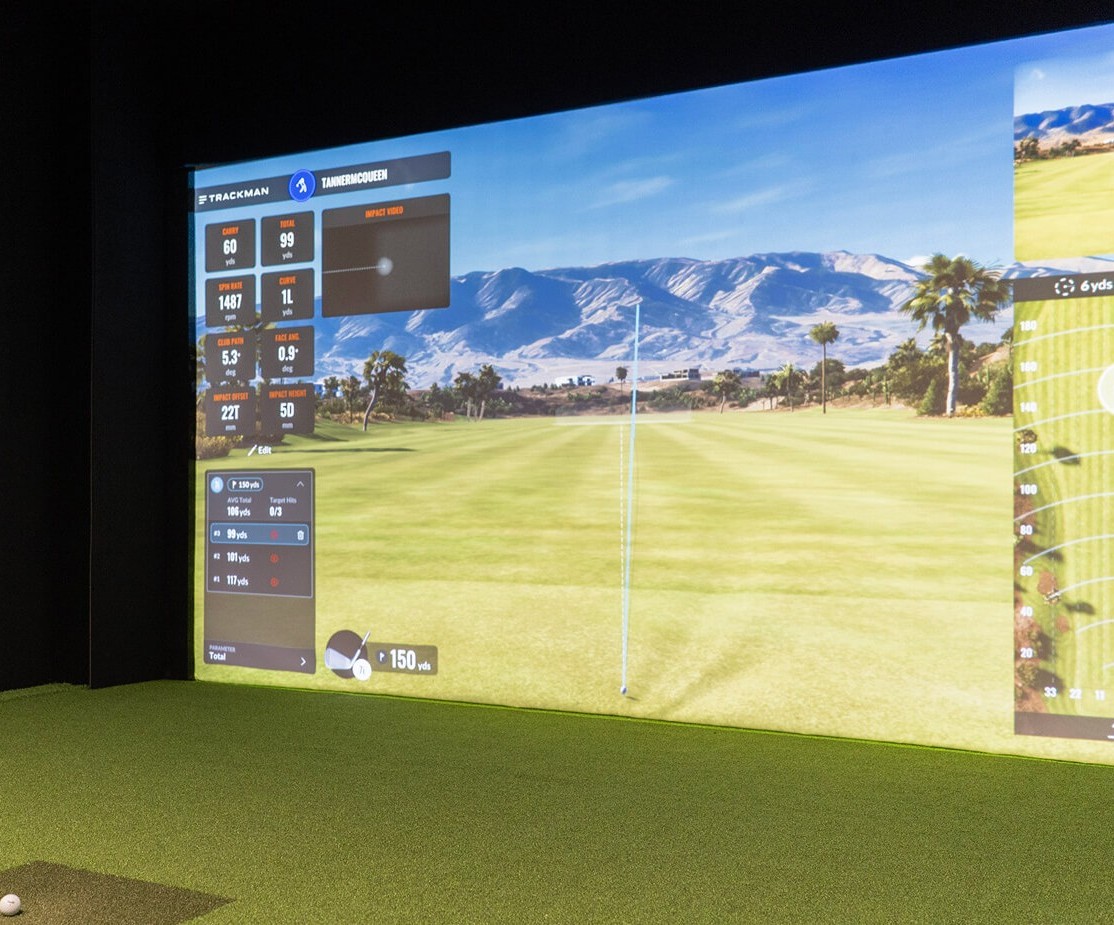Indoor golf simulator showing a digital golf course with swing data and stats displayed on screen.