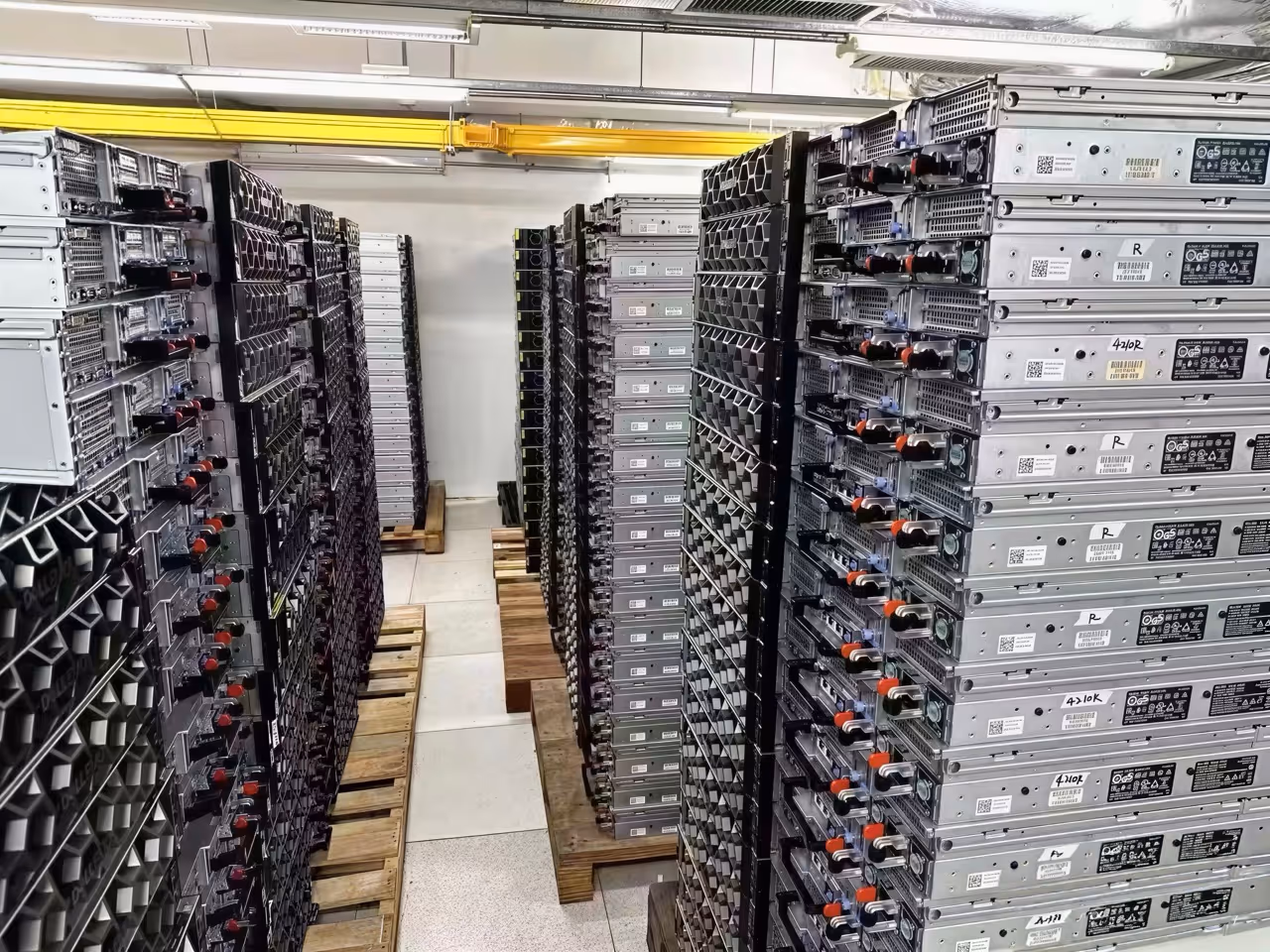 Rows of stacked, silver server racks in a data center, arranged on wooden pallets with visible ventilation and cabling.
