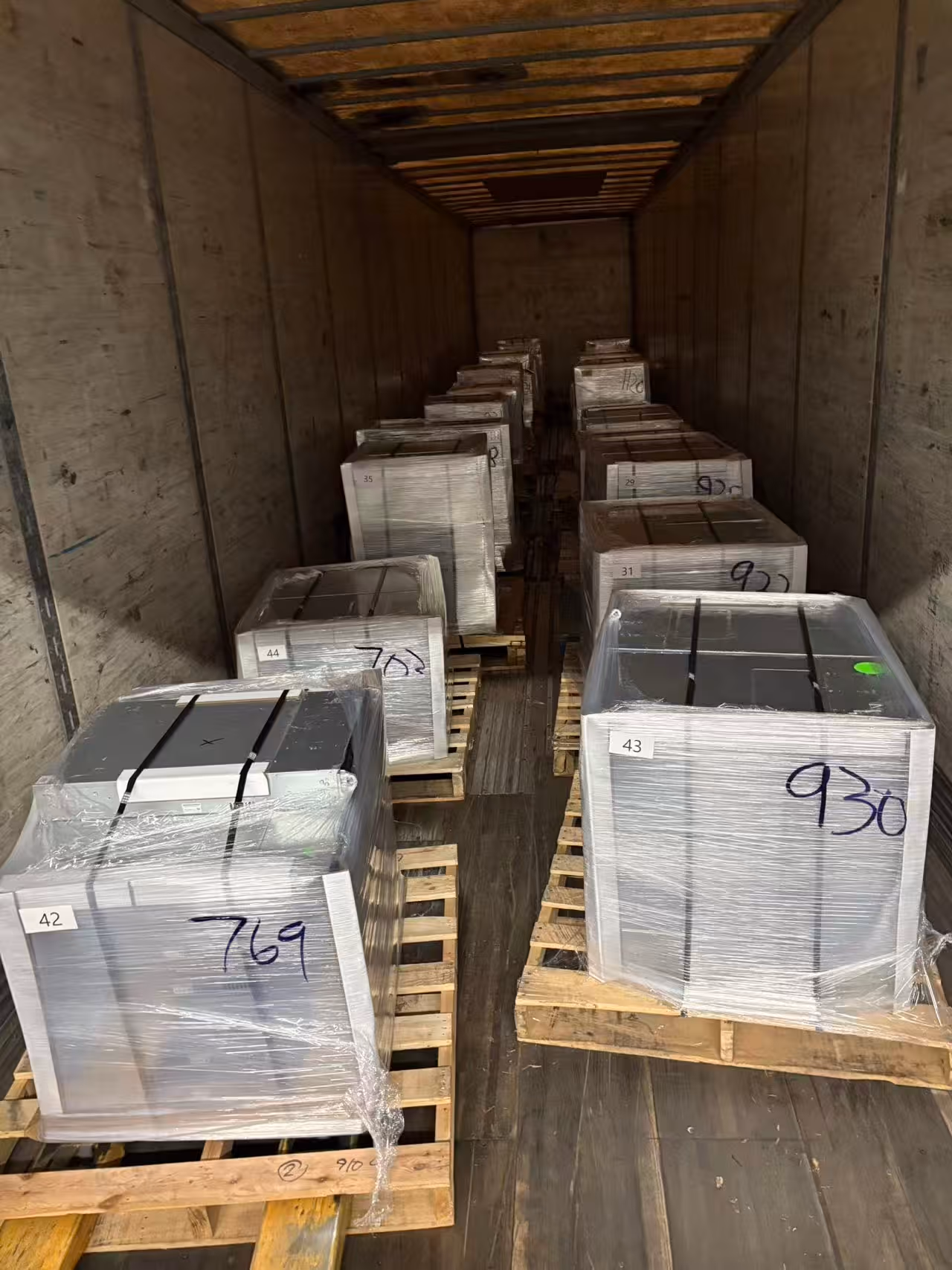 Wooden pallets loaded with shrink-wrapped boxed items stacked inside a trailer.