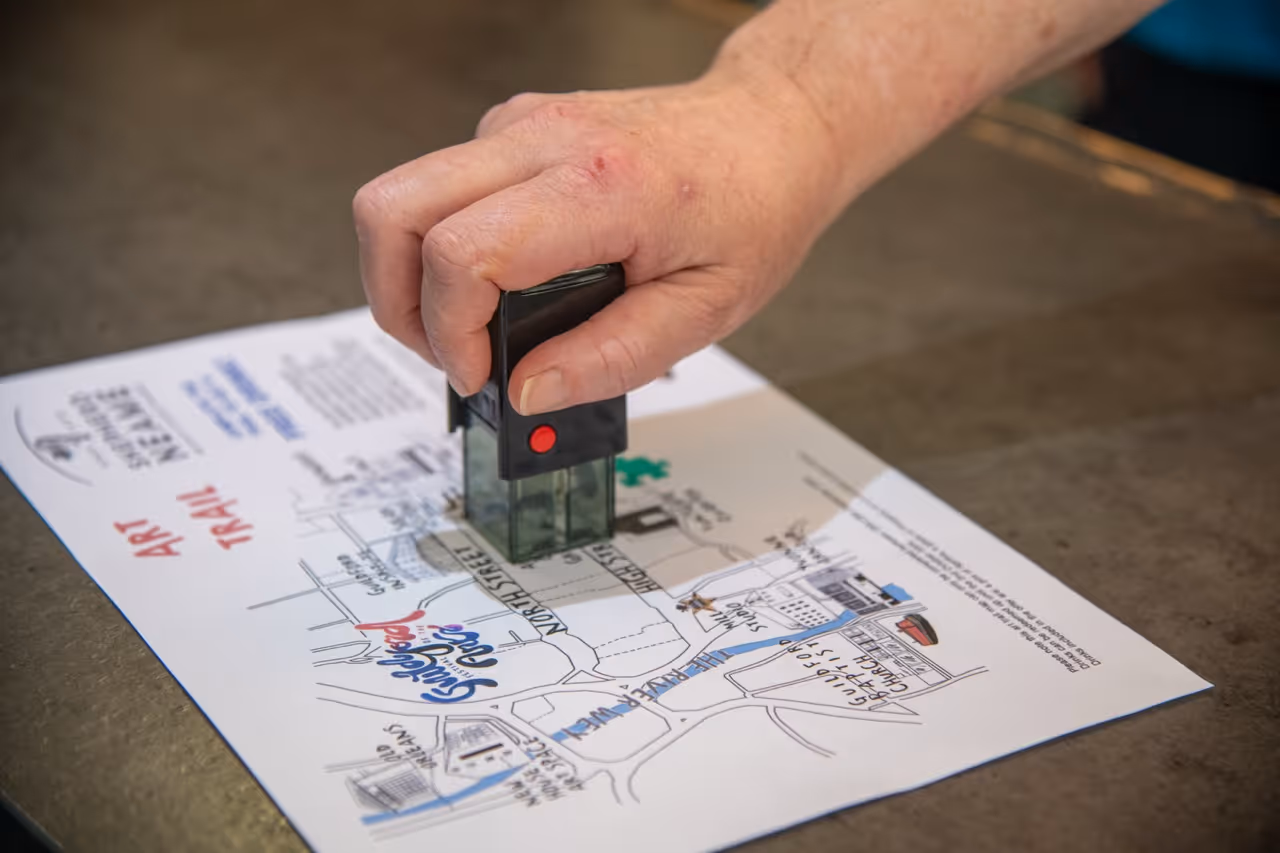 Hand stamping a paper map titled 'Art Trail' showing Guildford town layout and landmarks.