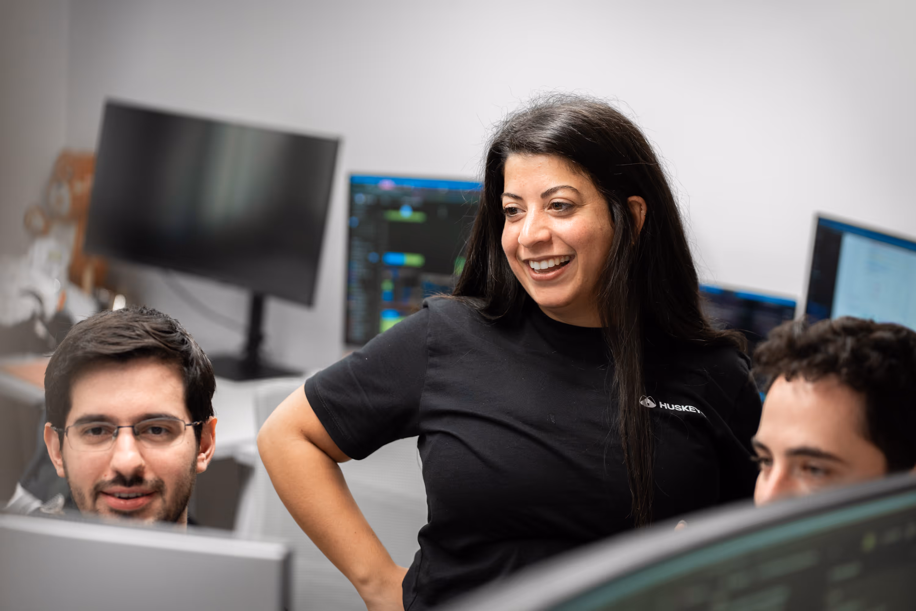 Three people collaborating and smiling while looking at computer screens in an office.