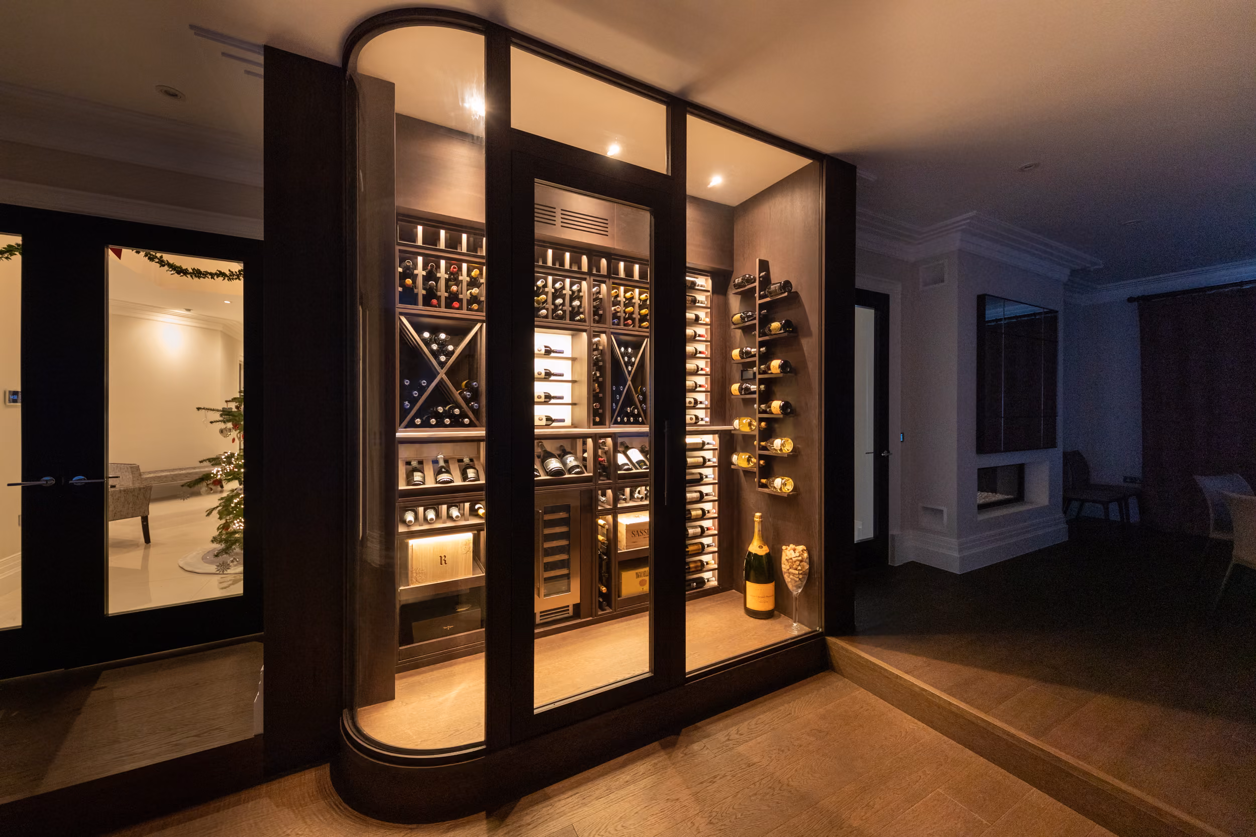 Small glazed wine room built into a hallway, with racking, a wine cabinet and feature lighting
