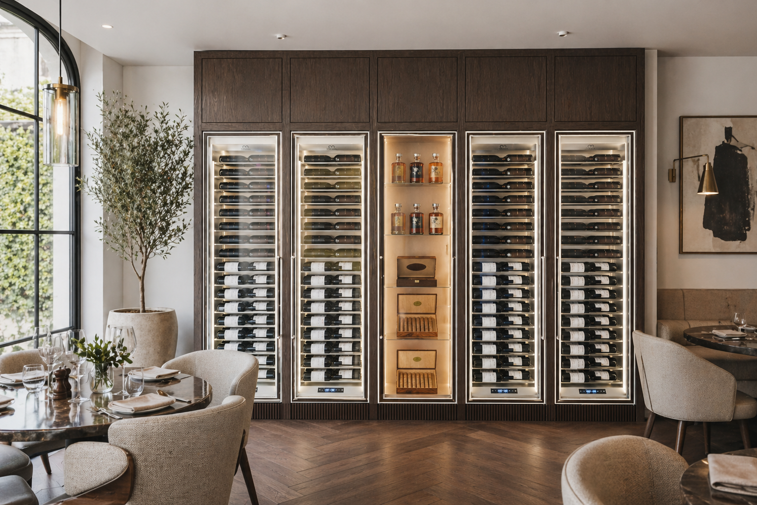 Bank of five glass-fronted wine cabinets set into a dark joinery surround in a daylit restaurant dining room, with one warm-lit central cabinet
