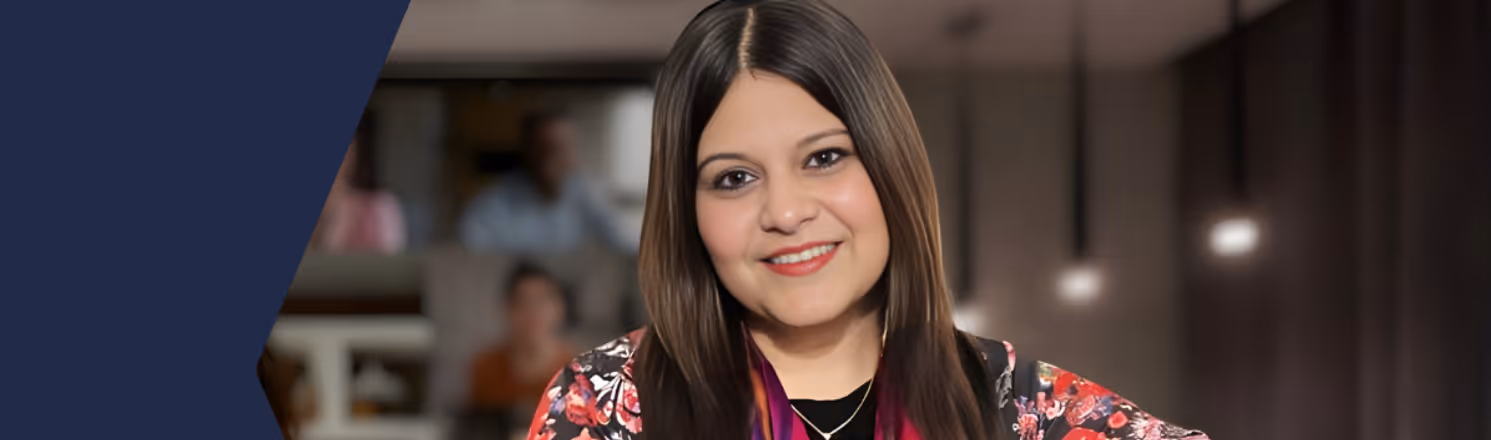 Woman with long brown hair wearing a floral jacket and smiling indoors with blurred background.