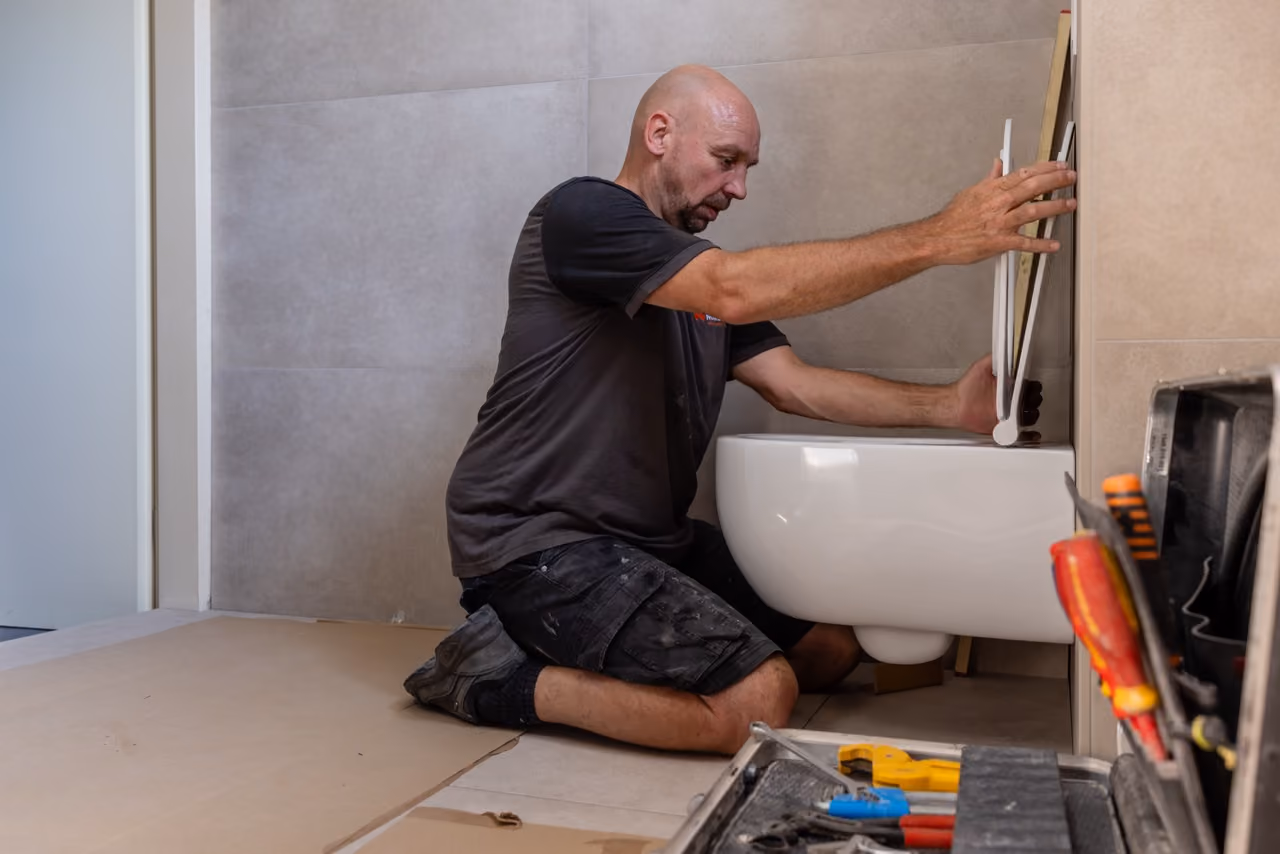 Installateur van Marboma monteert een hangend toilet in een badkamer met grijze wandtegels