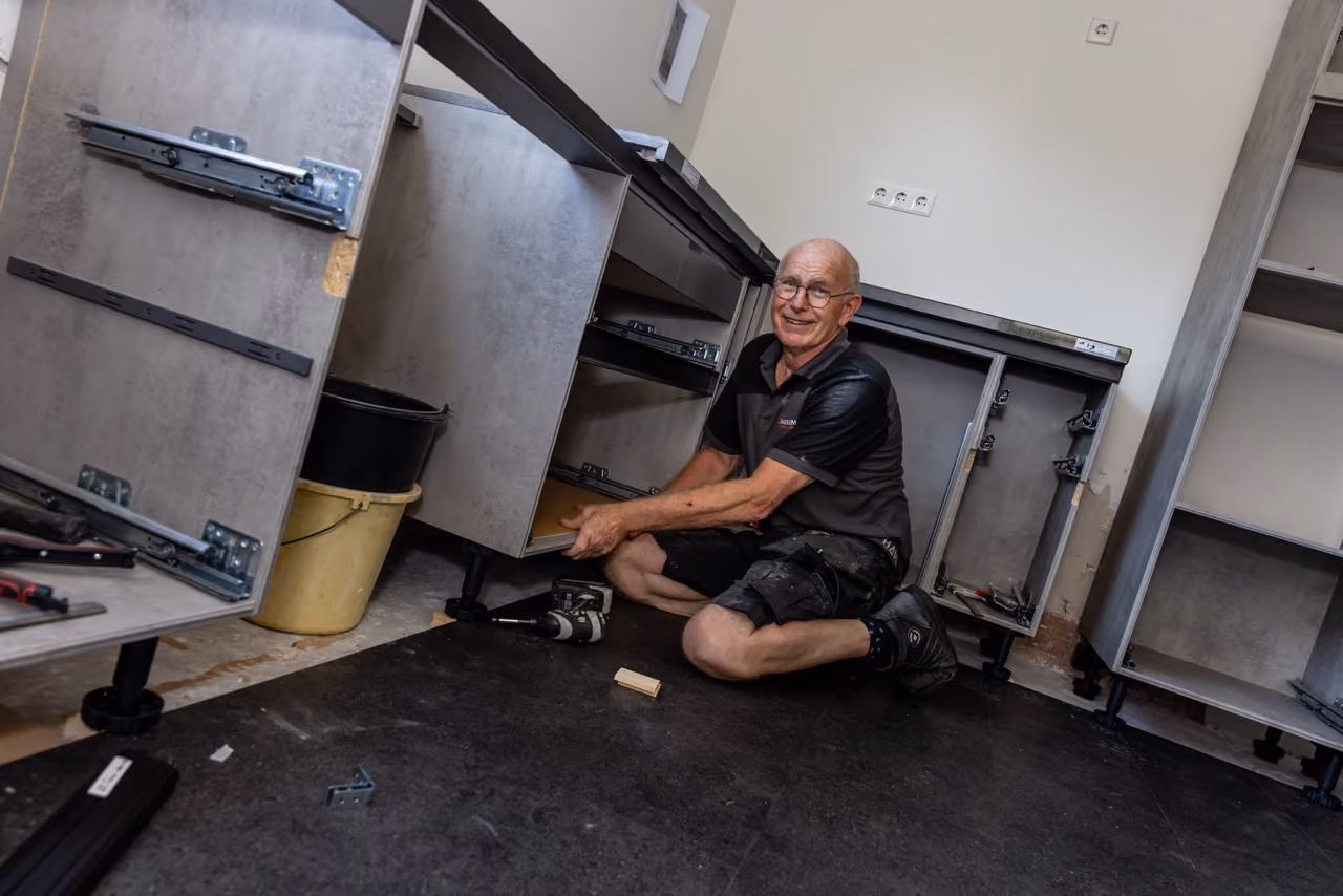 Monteur van Marboma zit op de vloer tussen de keukenkasten tijdens het plaatsen van een keuken